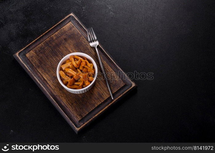 Canned mushrooms in a bowl on a dark background. Homemade pickled honey agarics mushrooms in a white bowl