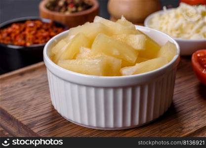 Canned pineapple chunks. Pineapple pieces on dark background. Canned pineapple chunks in a white bowl on a dark concrete background
