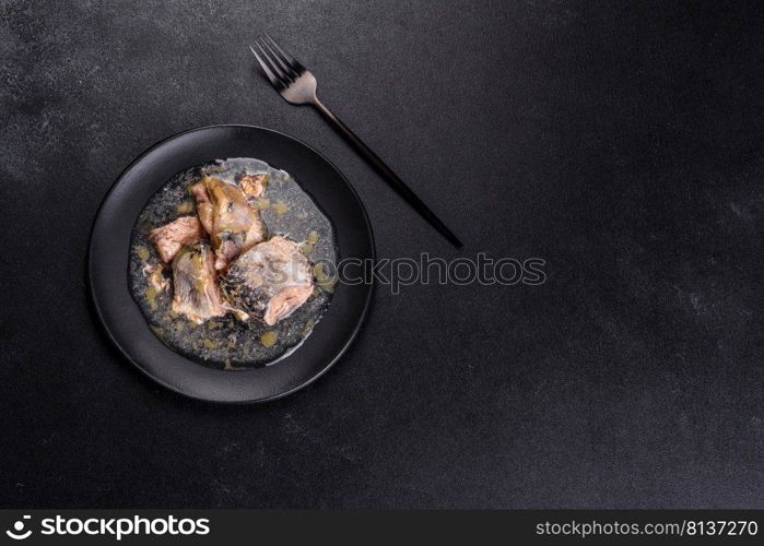 Canned sardine in oil on a black round plate against a dark concrete background. Making a delicious snack. Canned sardine in oil on a black round plate against a dark concrete background