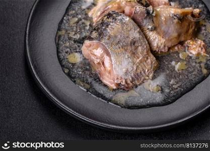 Canned sardine in oil on a black round plate against a dark concrete background. Making a delicious snack. Canned sardine in oil on a black round plate against a dark concrete background