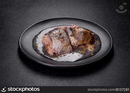 Canned sardine in oil on a black round plate against a dark concrete background. Making a delicious snack. Canned sardine in oil on a black round plate against a dark concrete background