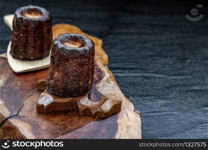 Canneles (Caneles) de Bordeaux Recipe is a small pastry with rum and vanilla on a wooden plate. Traditional French sweet dessert. tasty snacks. Oblique view from the top. Place for text.