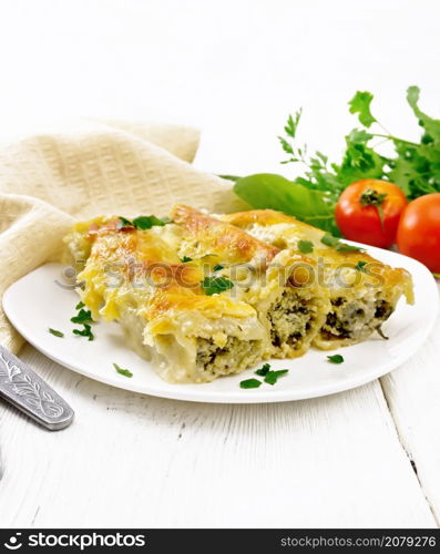 Cannelloni stuffed with cottage cheese and spinach with Bechamel sauce in a plate, napkin, tomatoes and parsley on a wooden board background