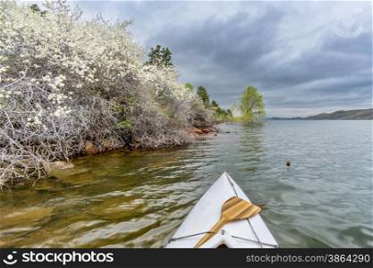 canoa bow with a wooden paddle on Horsetooth Rerservoir, springtime scenry with blooming bushes