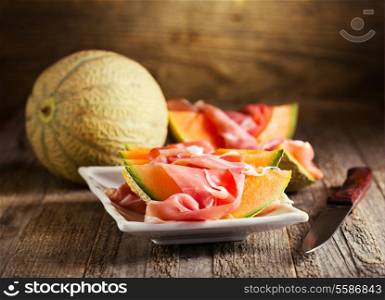 cantaloupe melon with prosciutto on wooden background