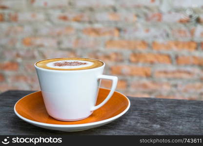 Cappuccino coffee in white cup on wooden table with old brick wall background