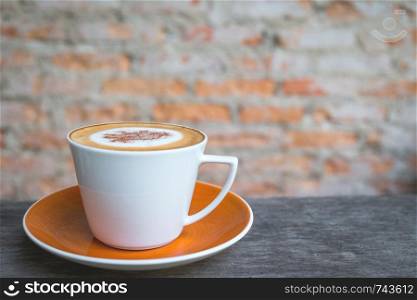 Cappuccino coffee in white cup on wooden table with old brick wall background