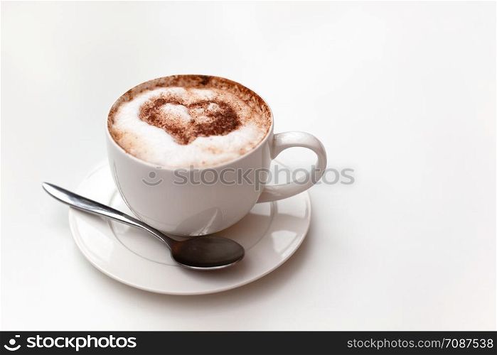 Cappuccino cup on white table background. Foam is decorated with cinnamon heart. Copy space. Top view, located at side of frame. Horizontal. Mock up for social media, food blog, lifestyle. Soft focus.