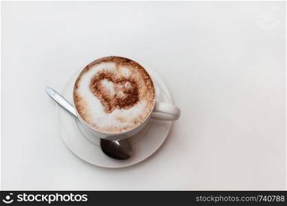 Cappuccino cup on white table background. Foam is decorated with cinnamon heart. Copy space. Top view, located at side of frame. Horizontal. Lactose free concept. Soft focus