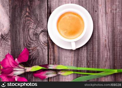 cappuccino in a white cup with a saucer on a gray wooden background, next to a red blossoming iris