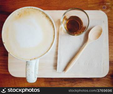 Cappuccino or latte coffee on wooden tray with syrup, retro filter effect