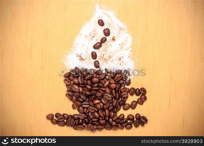 Cappuccino time. Roasted coffee beans placed in shape of cup and saucer with cinnamon white froth on wooden surface background