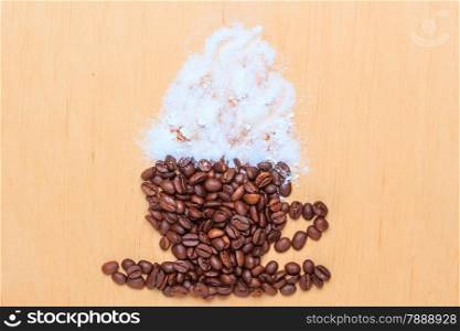 Cappuccino time. Roasted coffee beans placed in shape of cup and saucer with white froth on wooden surface background