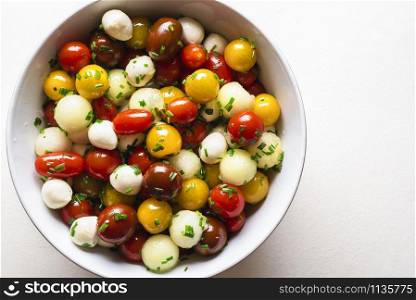 Caprese salad in bowl on white table. Flat lay of colorful salad close-up. Cherry tomatoes and mozzarella salad. Italian dinner. Mediterranian salad.