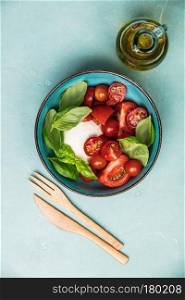 Caprese salad. Mozzarella cheese, tomatoes and basil herb leaves. Blue background. Top view