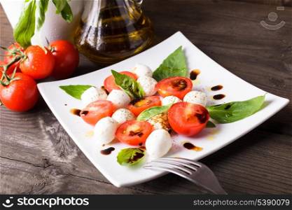 Caprese salad: tomato, mozzarella, basil leaves with olive oil and balsamico