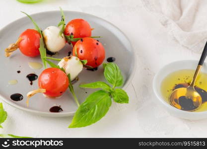 Caprese skewers with tomatoes, mozzarella balls, basil and spices on white table, closeup.  Italian homemade food and a healthy diet concept.