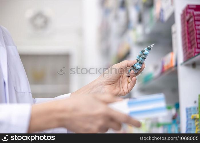capsule in the women pharmacist hand and medicine shelf background in pharmacy store Thailand