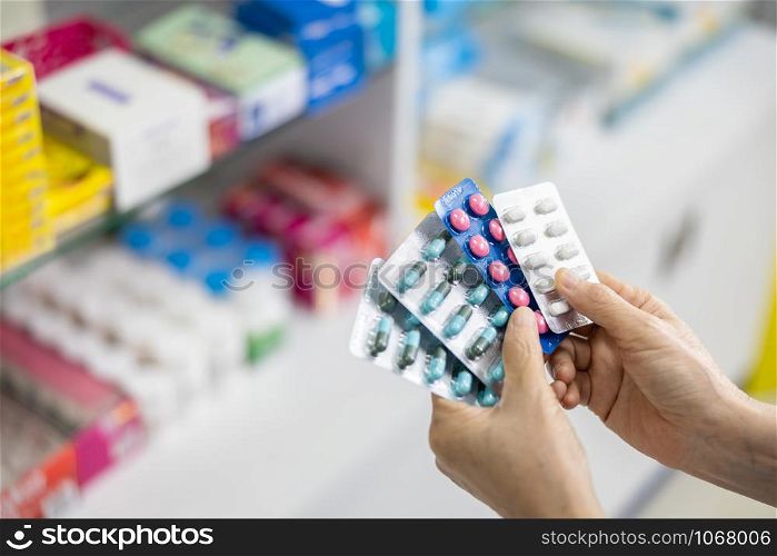 capsule in the women pharmacist hand and medicine shelf background in pharmacy store Thailand