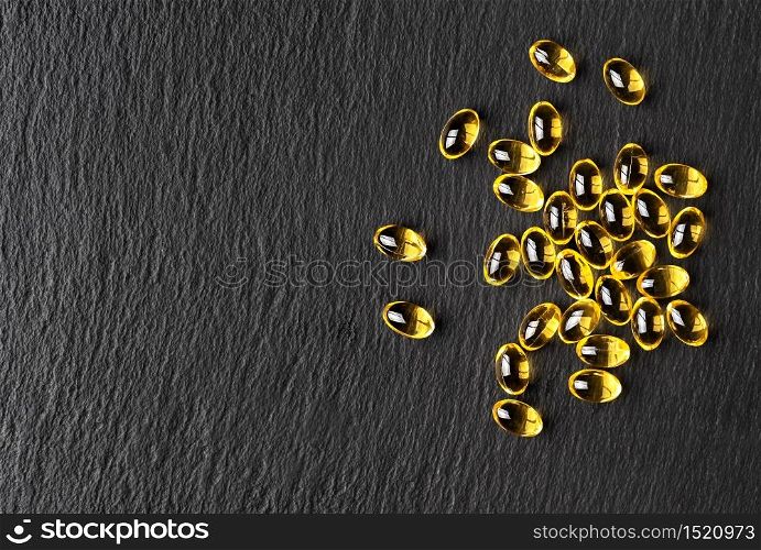 Capsules of fish oil (omega-3) on a black stone background. Flat layout with copy space for the recipe. Useful food supplements.