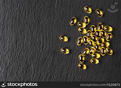 Capsules of fish oil (omega-3) on a black stone background. Flat layout with copy space for the recipe. Useful food supplements.