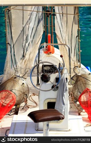 Captain s bridge, a steering wheel, fishing nets and a captain s t-shirt on the running lever of a small old fishing boat that sways on the waves of the open sea in blur.. View of the captain s bridge and the helm of a small old fishing schooner with hanging fishing nets.