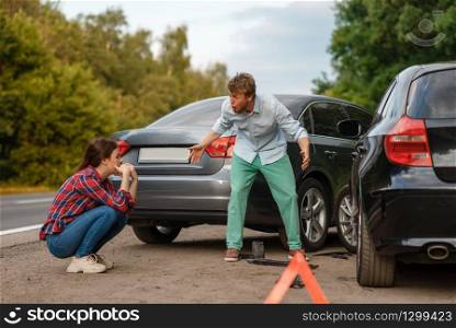 Car accident on road, male and female drivers are sorted out. Automobile crash, emergency stop sign. Broken automobile or damaged vehicle, auto collision on highway