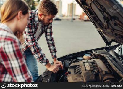 Car breakdown concept, sad couple against open hood. Female driver and mechanic of emergency service looks at the broken vehicle engine. Car breakdown concept, couple against open hood