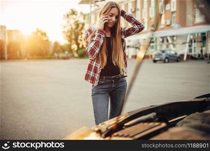 Car breakdown concept, sad woman against open bonnet on the roadside. Female driver looks at the broken vehicle engine. Car breakdown, sad woman against open bonnet