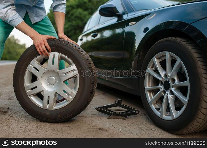 Car breakdown, man puts the spare tire. Broken automobile or problem with vehicle, trouble with punctured auto tyre on highway