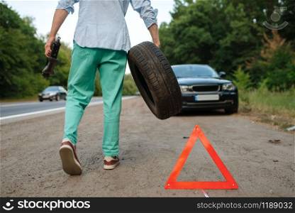 Car breakdown, man puts the spare tyre. Broken automobile or problem with vehicle, trouble with punctured auto tire on highway. Car breakdown, man puts the spare tyre