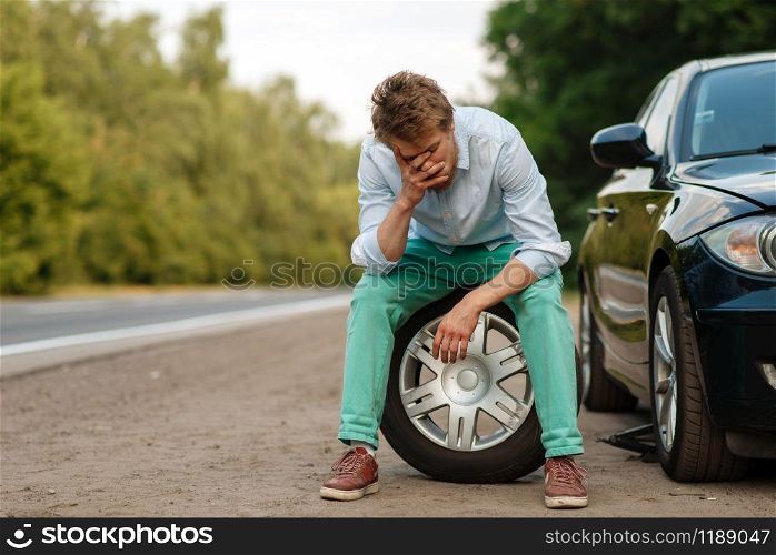 Car breakdown, tired man sitting on spare tyre. Broken automobile or problem with vehicle, trouble with punctured auto tire on highway. Car breakdown, tired man sitting on spare tyre
