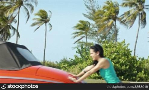 Car breakdown: two beautiful young women laughing while pushing broken down red convertible vintage car