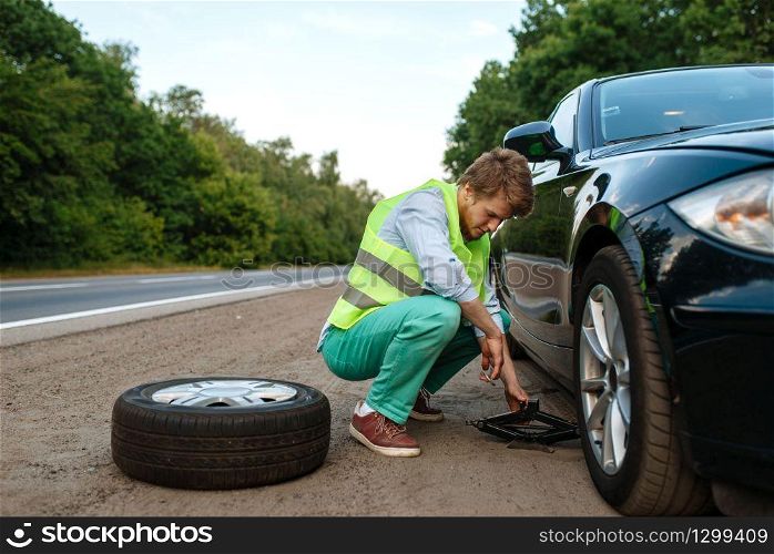Car breakdown, young man repairing flat tyre. Broken automobile or problem with vehicle, trouble with punctured auto tire on highway