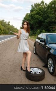 Car breakdown, young woman puts the spare tyre. Broken automobile or problem with vehicle, trouble with punctured auto tire on highway. Car breakdown, young woman puts the spare tyre