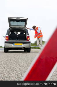 Car broken down on the freeway, with the driver calling assistant, leaning, and the suggestion of a warning triangle in front