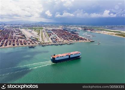 car carrier sailing on the green sea and international shipping container port background aerial view