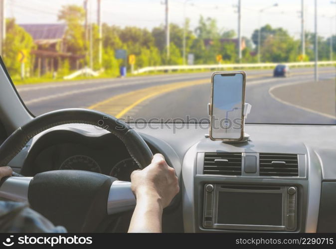 Car driver using smartphone with GPS map navigation application while driving on curve way on country road, view from inside car
