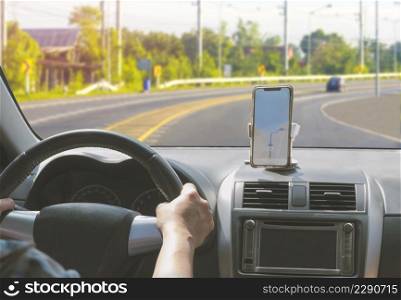 Car driver using smartphone with GPS map navigation application while driving on curve way on country road, view from inside car
