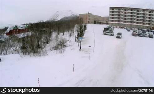 Car driving out the parking lot by the hotel and heading to the road to mountains. Shot is made using the drone