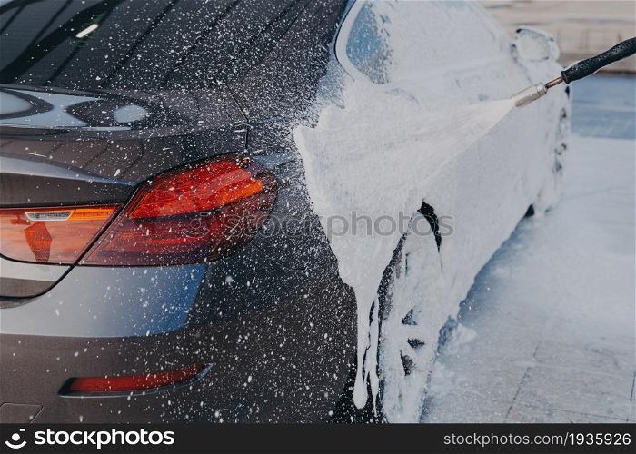 Car exterior cleaning. Applying snow foam on dirty auto surface from high-pressure washer at carwash station outdoors, worker spraying suds on auto with special sprayer. Car exterior cleaning, applying snow foam on dirty auto surface from high-pressure washer