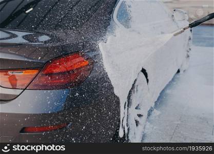 Car exterior cleaning. Applying snow foam on dirty auto surface from high-pressure washer at carwash station outdoors, worker spraying suds on auto with special sprayer. Car exterior cleaning, applying snow foam on dirty auto surface from high-pressure washer