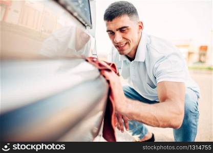 Car exterior polishing on carwash station. Man rubbing vehicle bumper with automobile polish. Car exterior polishing on carwash station