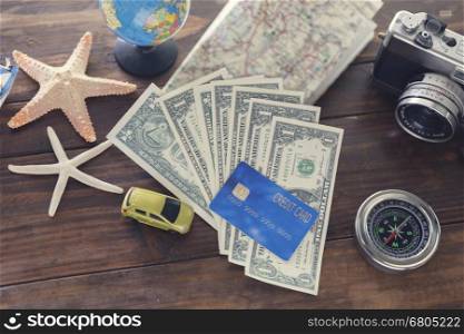 car figurine, compass, credit card, banknote money, globe, camera, map, ship and starfish on wooden table for use as traveling concept (vintage tone and selected focus)