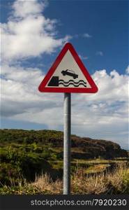 Car going off edge of land into water. United Kingdom triangular warning sign, warning of quayside or river bank.