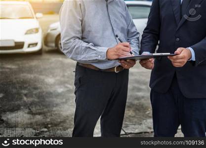 Car insurance agent send a pen to his customers sign the insurance form on clipboard while examining car after accident claim.