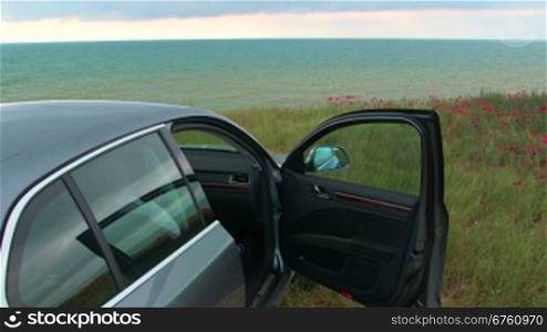Car is parked with opened door at the seaside in a cloudy day