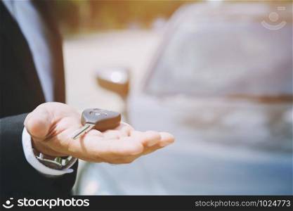Car key, businessman handing over gives the car key to the other man on car background.