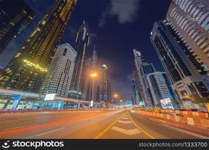 Car light trails on road or street in Dubai Downtown skyline and highway, United Arab Emirates or UAE. Financial district and business area in smart urban city. Skyscraper buildings at night.