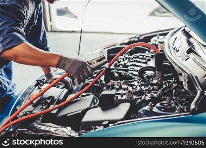 Car mechanic holding battery electricity trough cables jumper and checking to maintenance vehicle by customer claim order in auto repair shop garage. Repair service. People occupation and business job